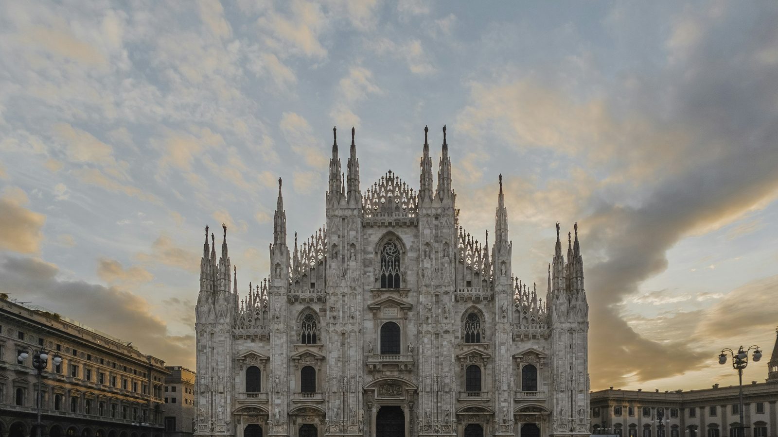 The Gothic facade of Milan Cathedral (Duomo di Milano) on Piazza del Duomo under a soft orange and blue evening sky