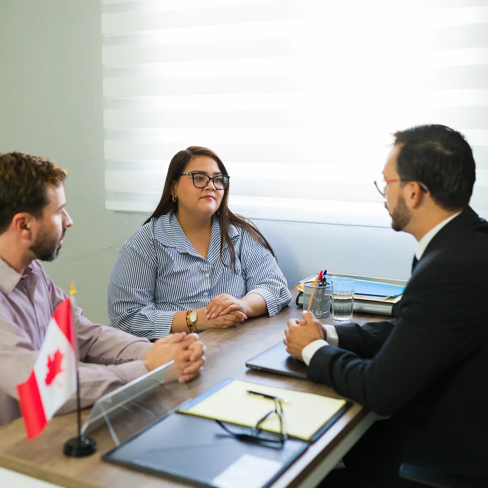 Three people discussing documents beside a Canadian flag.