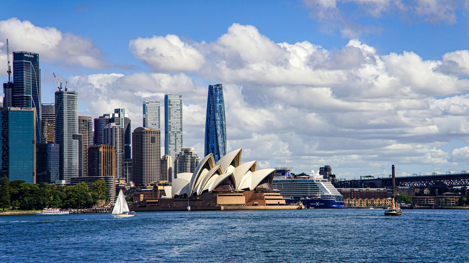 The Sydney Opera House and the city skyline seen from the harbour, with a sailboat and a cruise ship