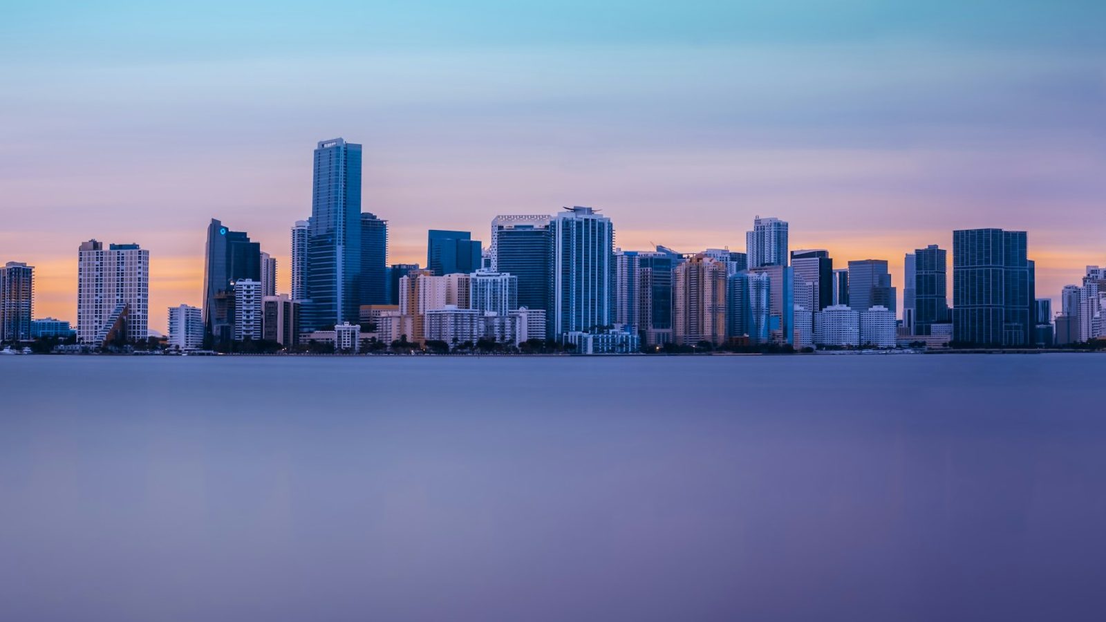 The downtown Miami and Brickell skyline across the calm water of Biscayne Bay under a pink and orange sky