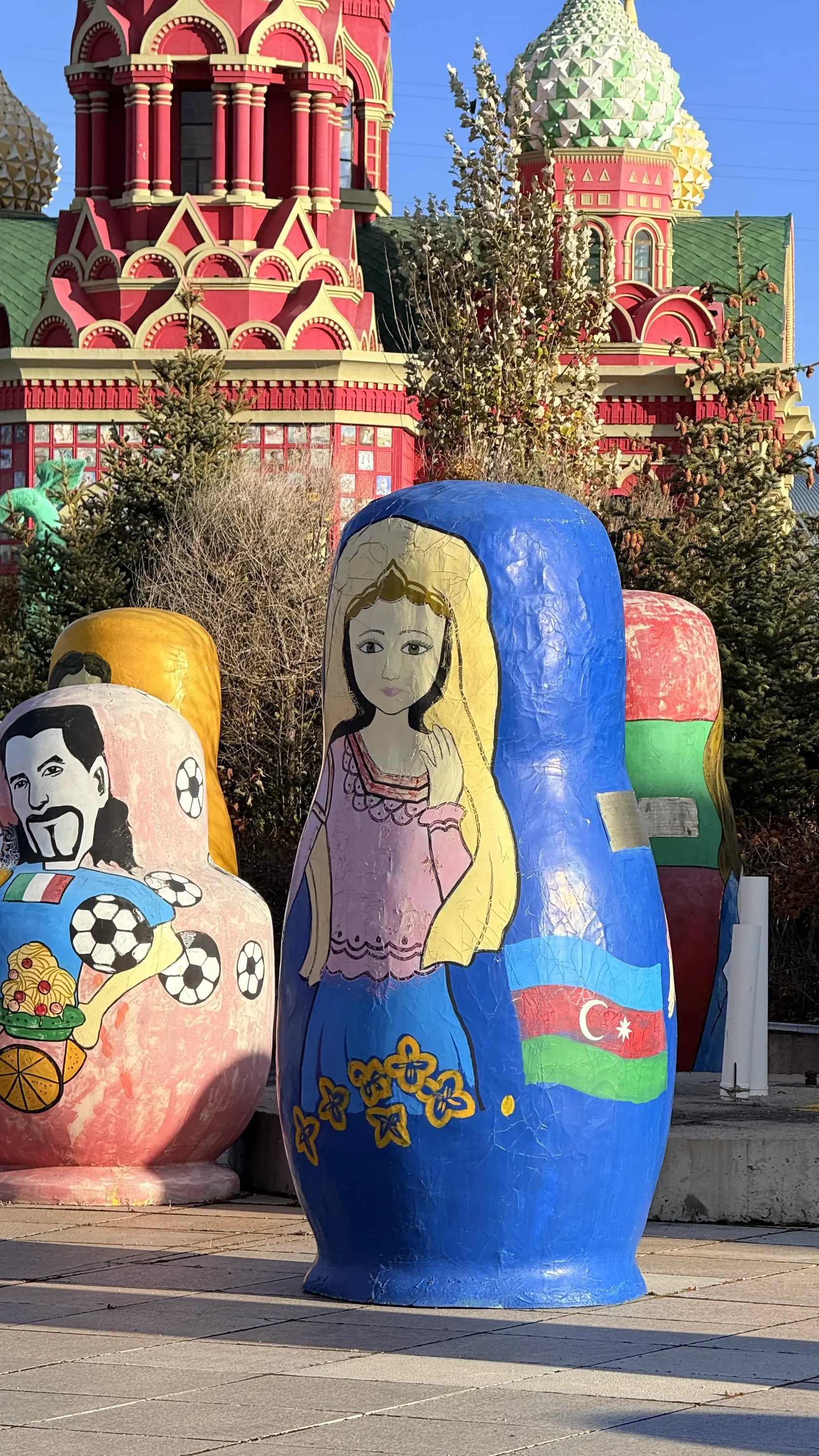 Высокая синяя Матрёшка с нарисованной девушкой и флагом среди других фигур