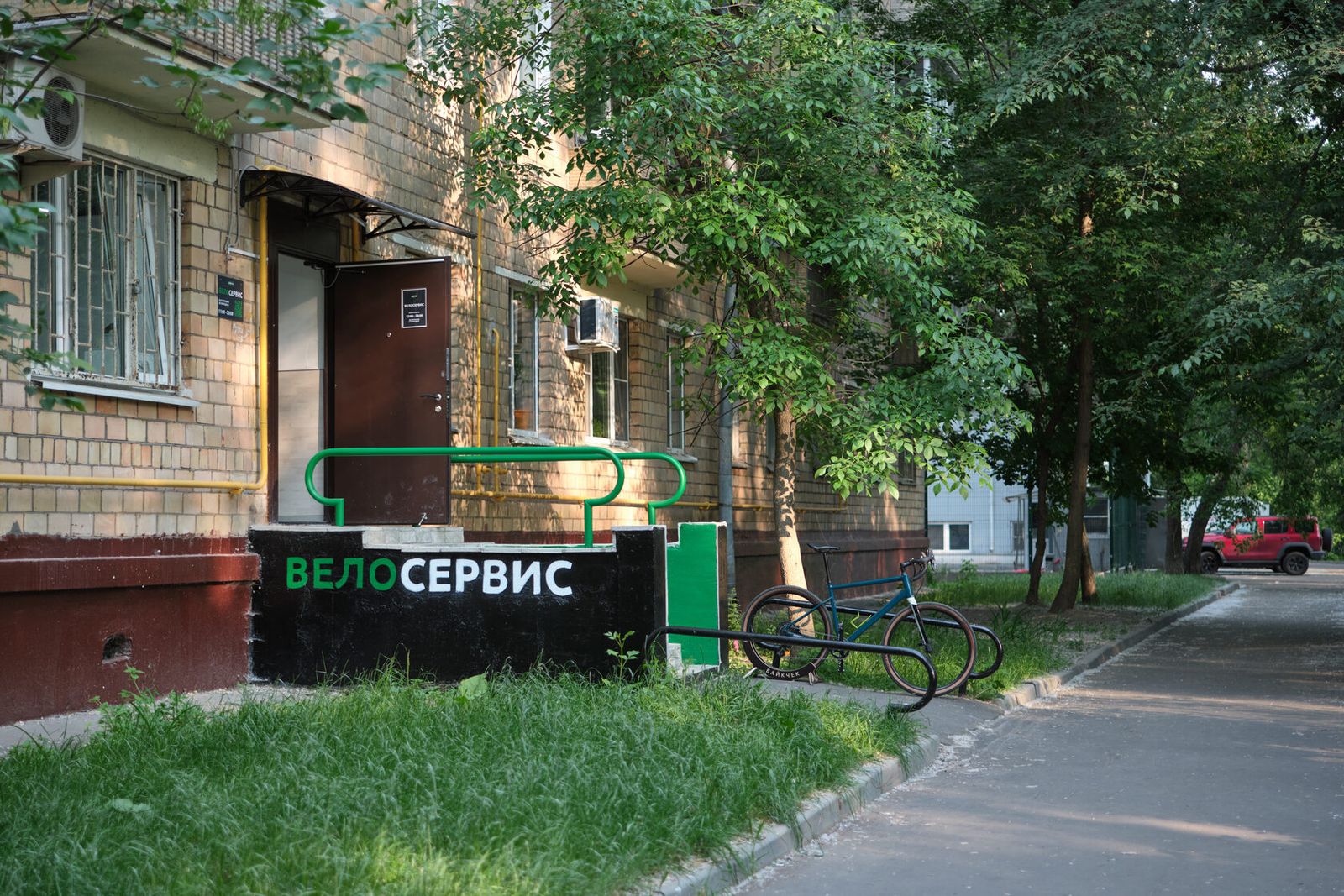 Вход в мастерскую «Байкчек – Хорошёво»: вывеска «Велосервис», зелёные перила и велопарковка