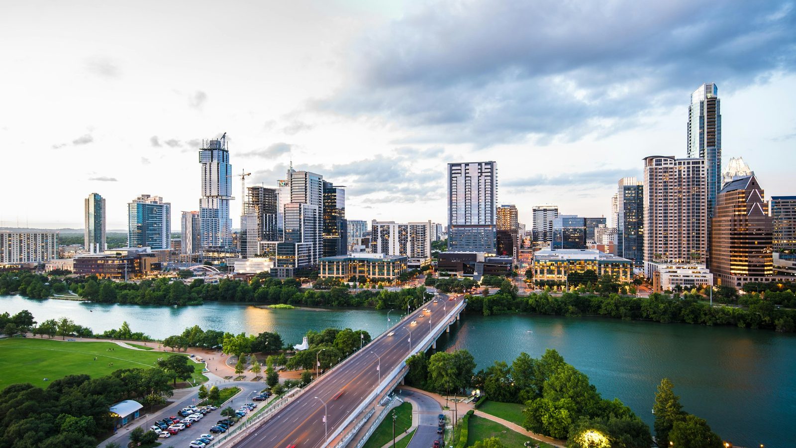 Aerial view of downtown Austin, Texas, with glass towers above Lady Bird Lake and cars on the Congress Avenue Bridge at dusk