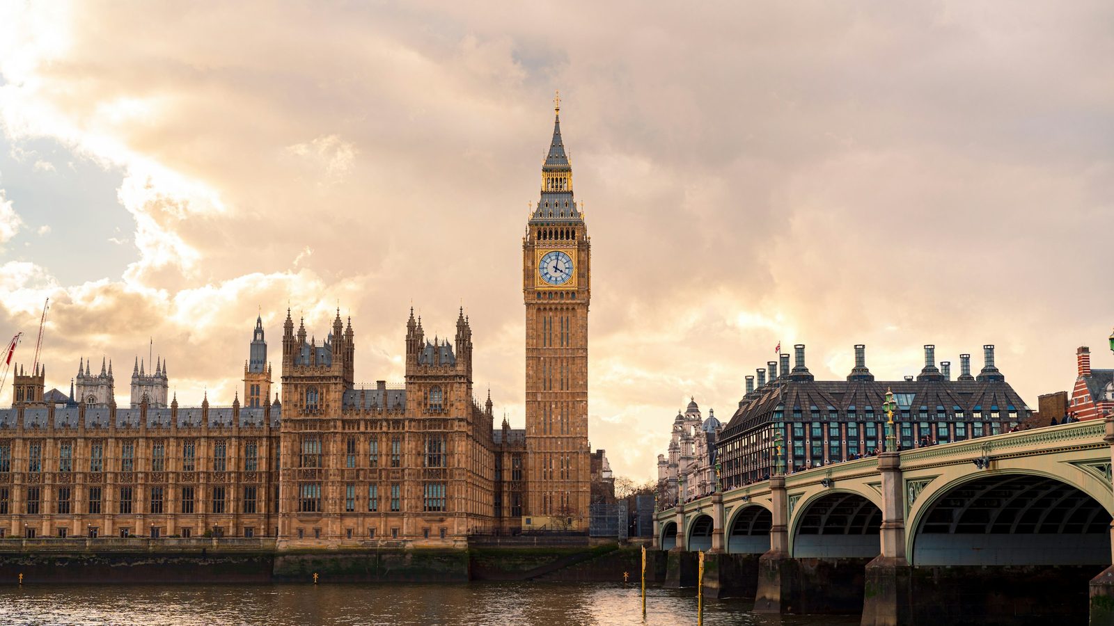 The Houses of Parliament and the Elizabeth Tower (Big Ben) in London beside Westminster Bridge and the River Thames under a cloudy golden sky