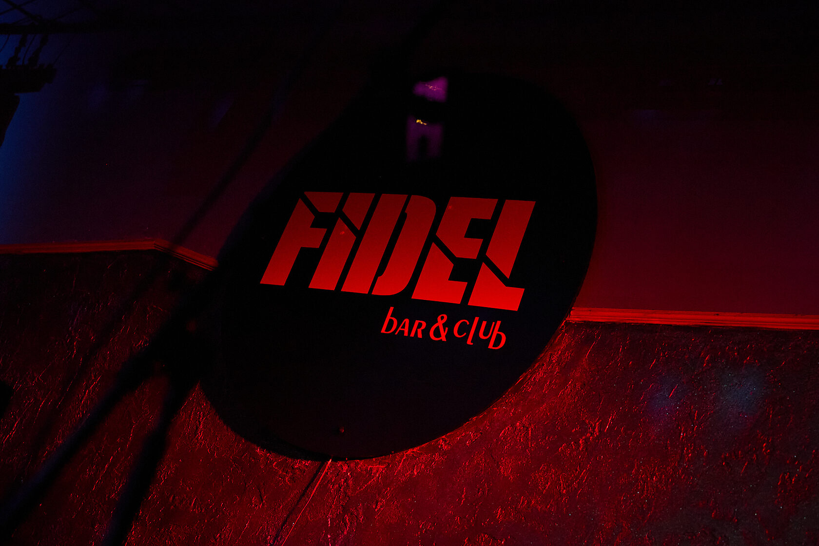 Логотип Fidel Bar and Club в красной подсветке на стене