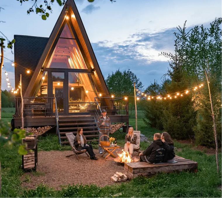 A-frame дом с гирляндами и костровой зоной вечером