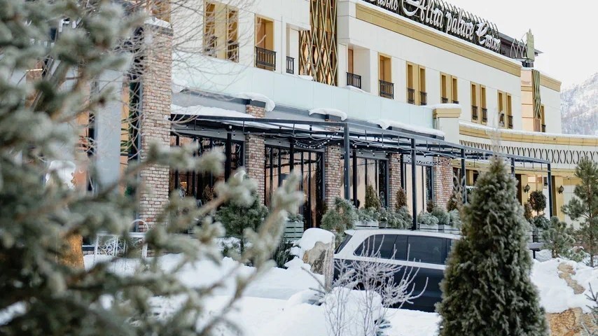 Отель Altai Palace 4* на курорте «Сибирская Монета» зимой: заснеженные ели у входа