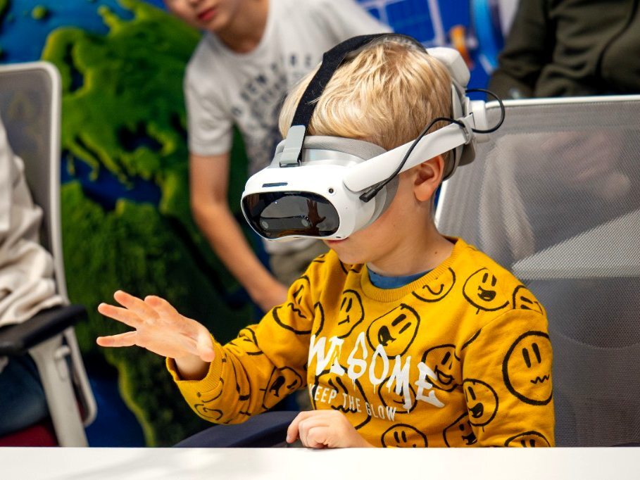 Мальчик в VR-шлеме на уроке тянется рукой к виртуальным объектам