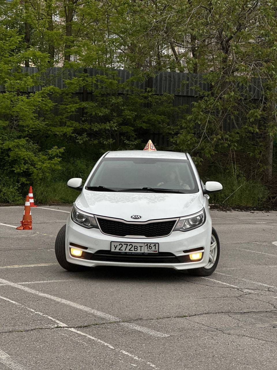 Белый учебный Kia Rio с включённым светом на площадке