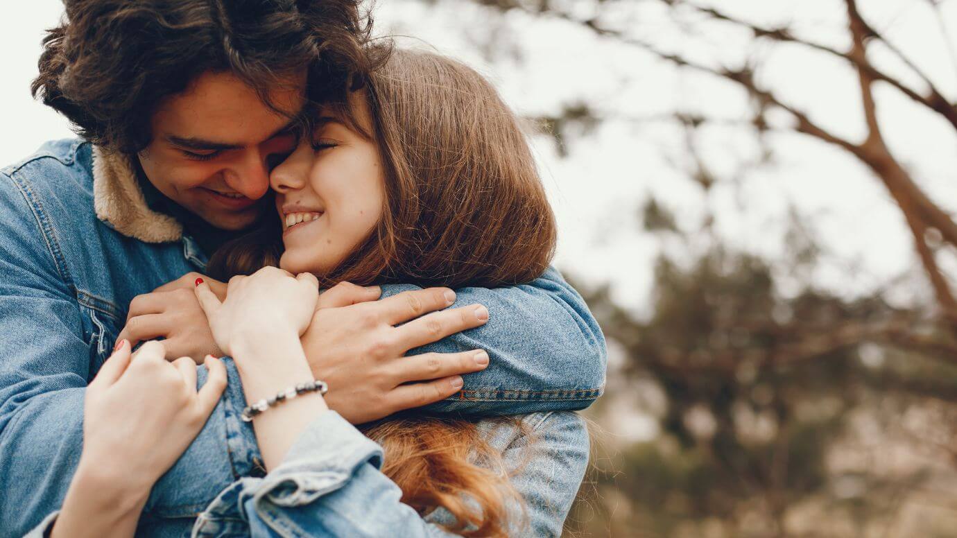 A brunette woman and man hugging in a city garden smiling