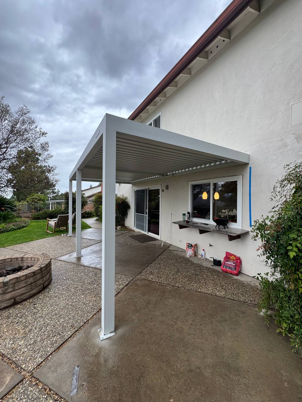Finished white wall-mounted aluminum pergola above the same concrete backyard patio in Fountain Valley