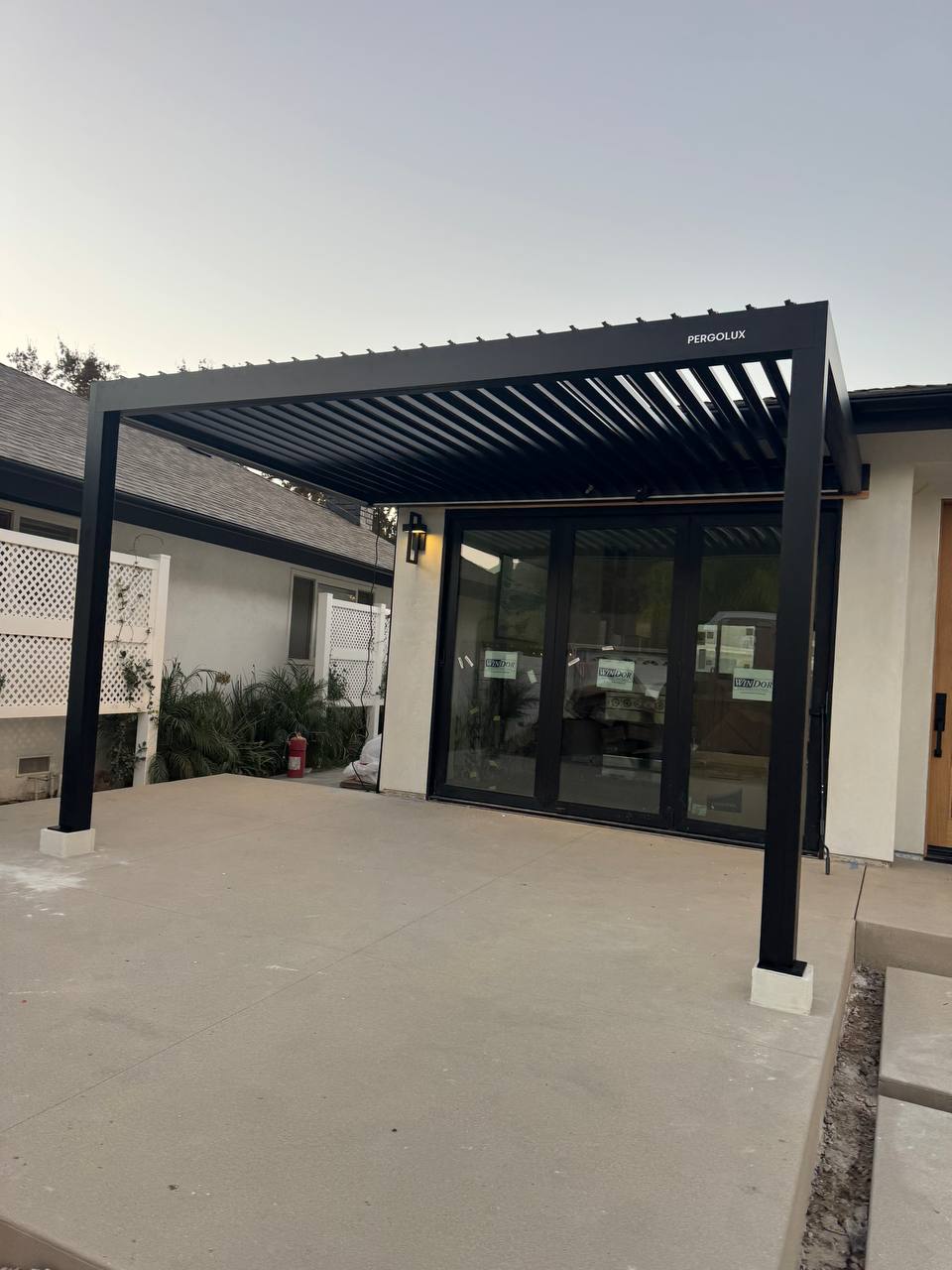 Front view of the finished pergola with open louvers above the glass patio doors.