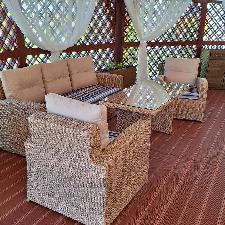 Лаунж-комплект Malacca из экоротанга с мягкими бежевыми подушками на террасе загородного комплекса.