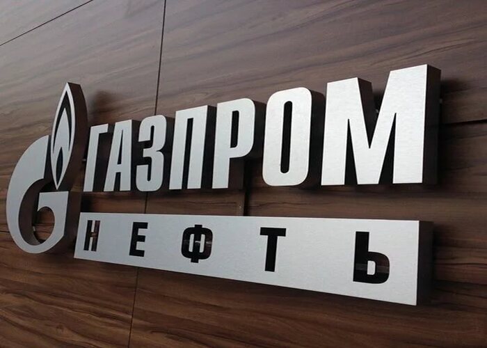 Серебристый логотип и буквы ГАЗПРОМ НЕФТЬ на деревянной стене