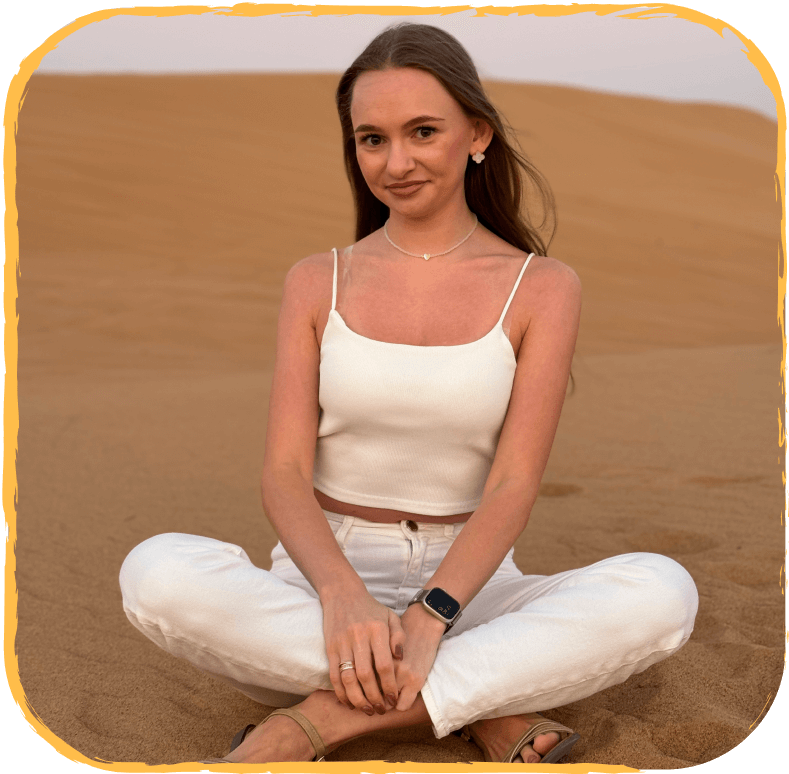 девушка шатенка в белом топе и джинсах сидит в позе лотоса в пустыне