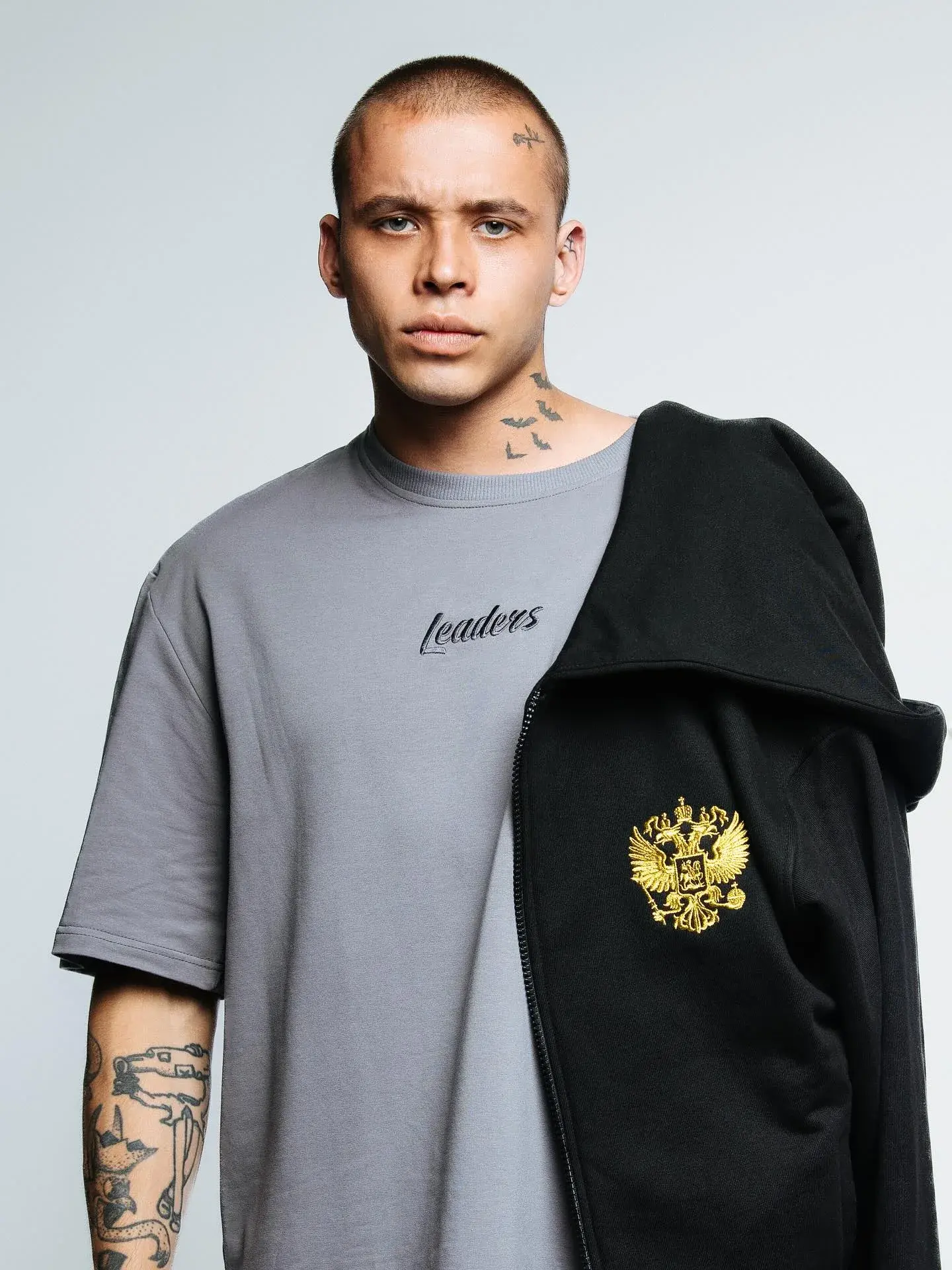 Модель в серой футболке Leaders Wear с чёрной верхней одеждой и гербом России.