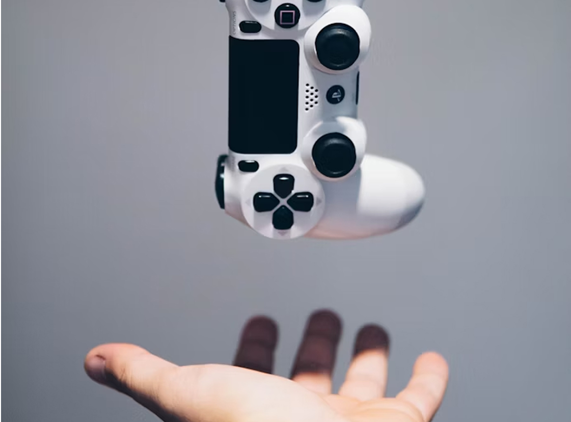 картинка о геймификации в продажах: консольный геймпад парит над раскрытой ладонью