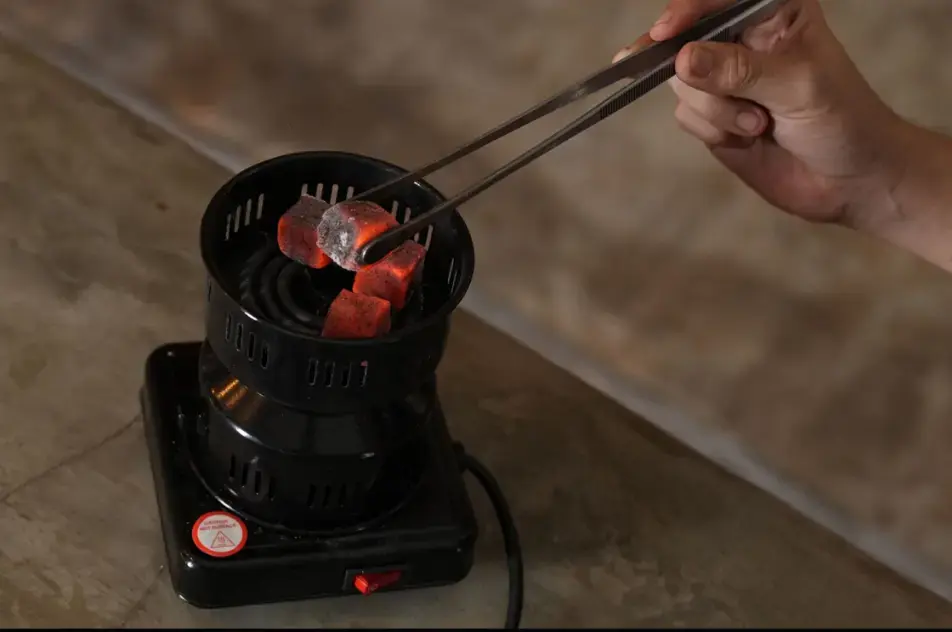 Heating natural coconut charcoal cubes on an electric coil burner until they are glowing red and ash-grey.
