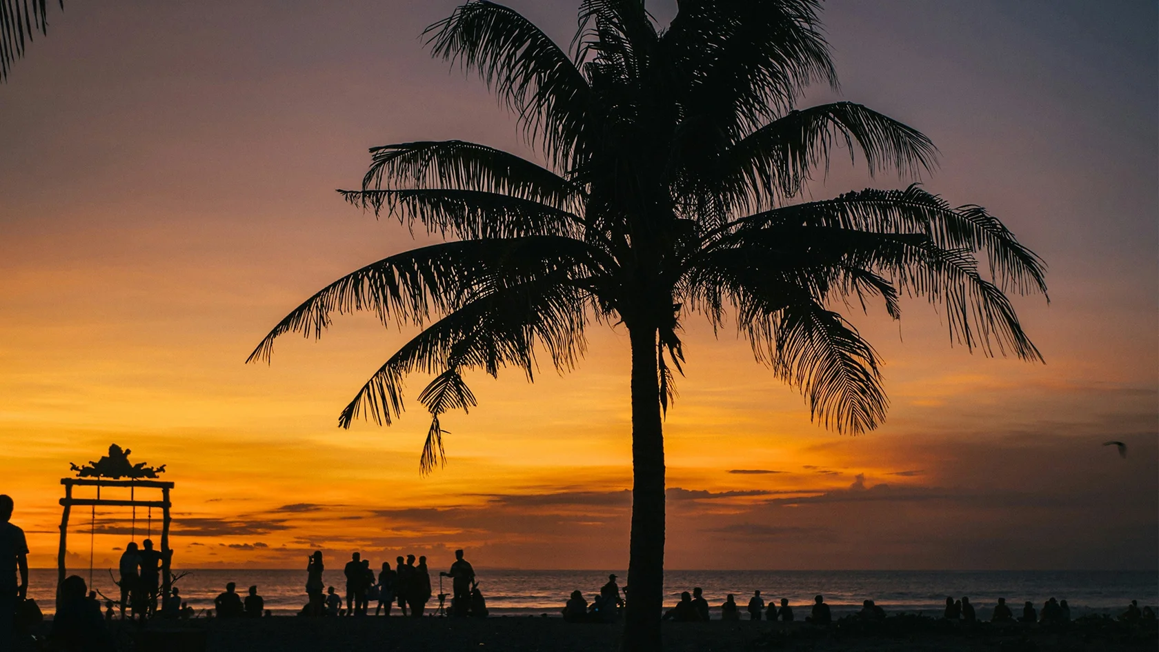 Silhouettes of people enjoying a vibrant orange sunset on a Bali beach setting the perfect scene for discovering what happens in Bali on Wednesday.