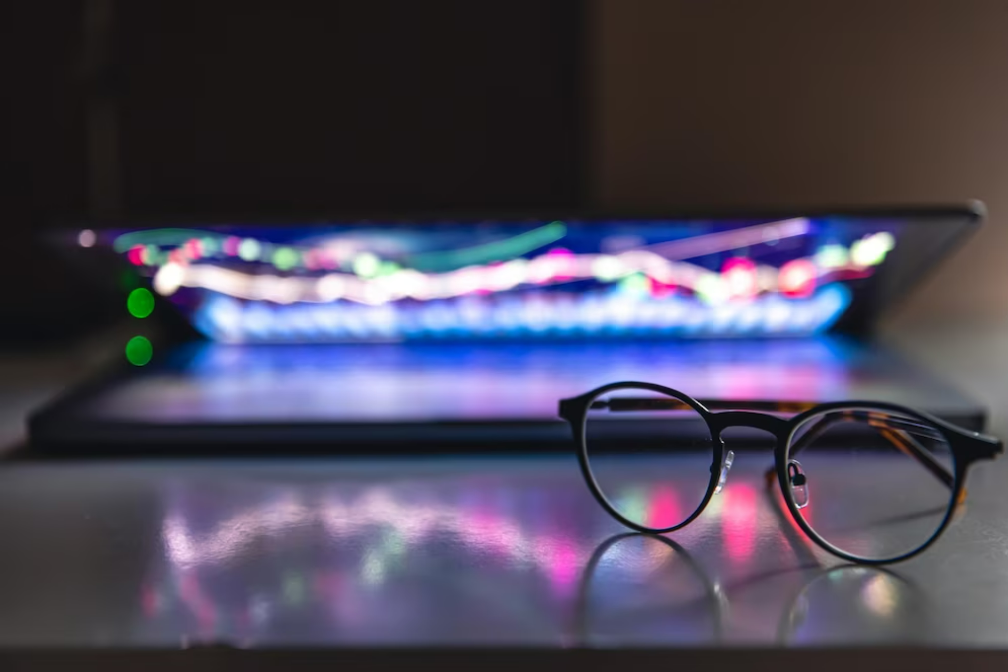 A laptop with crypto chart patterns and statistics and glasses