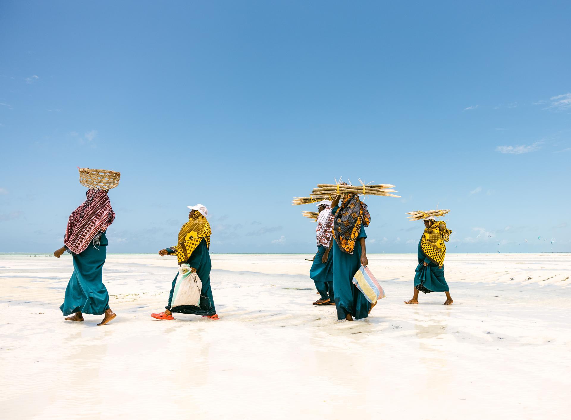 Tanzania (Zanzibar) | Samir Satchu. Wrapped in traditional kangas, women walk along the shore at low tide to harvest seaweed, a key source of income and independence.