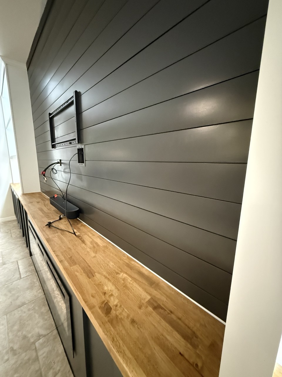 Black horizontal shiplap and natural wood countertop prepared for integrated TV equipment in a custom entertainment center
