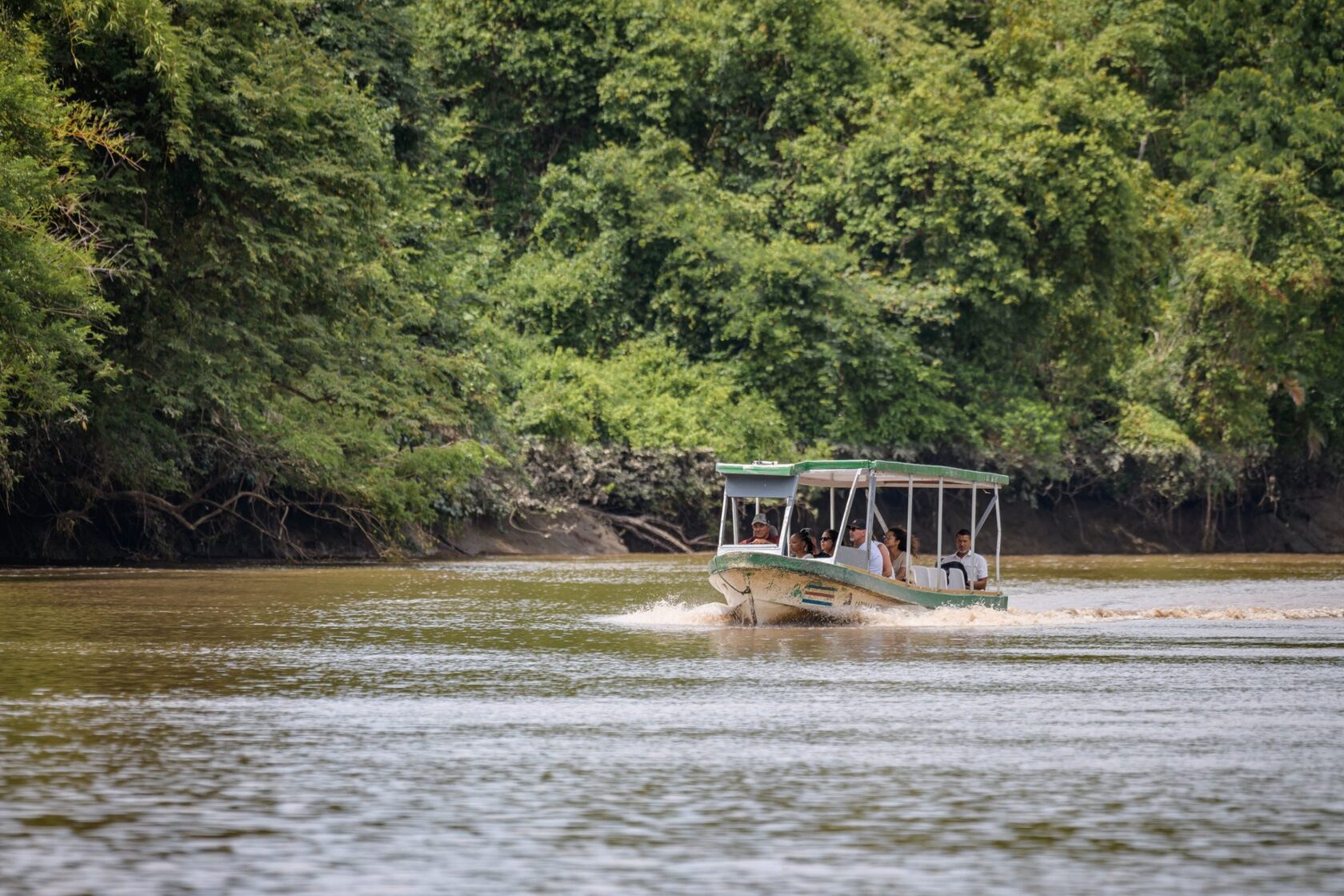 Covered tour boat on the Tempisque River beside forest