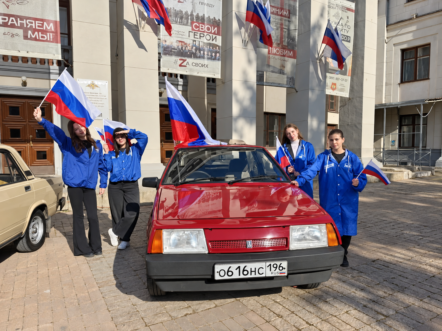 Участницы мероприятия с флагами рядом с красным автомобилем