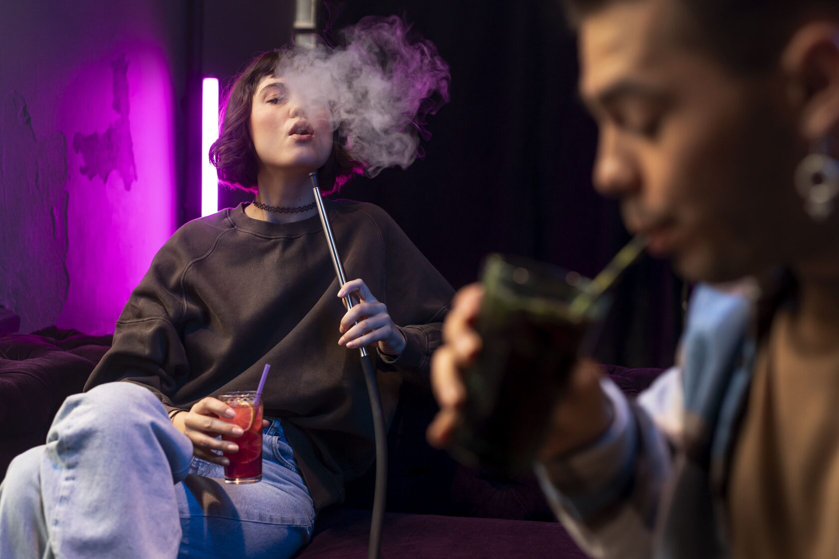 A girl smoking a hookah in a relaxed setting, focusing on her calm expression and gracefully released smoke