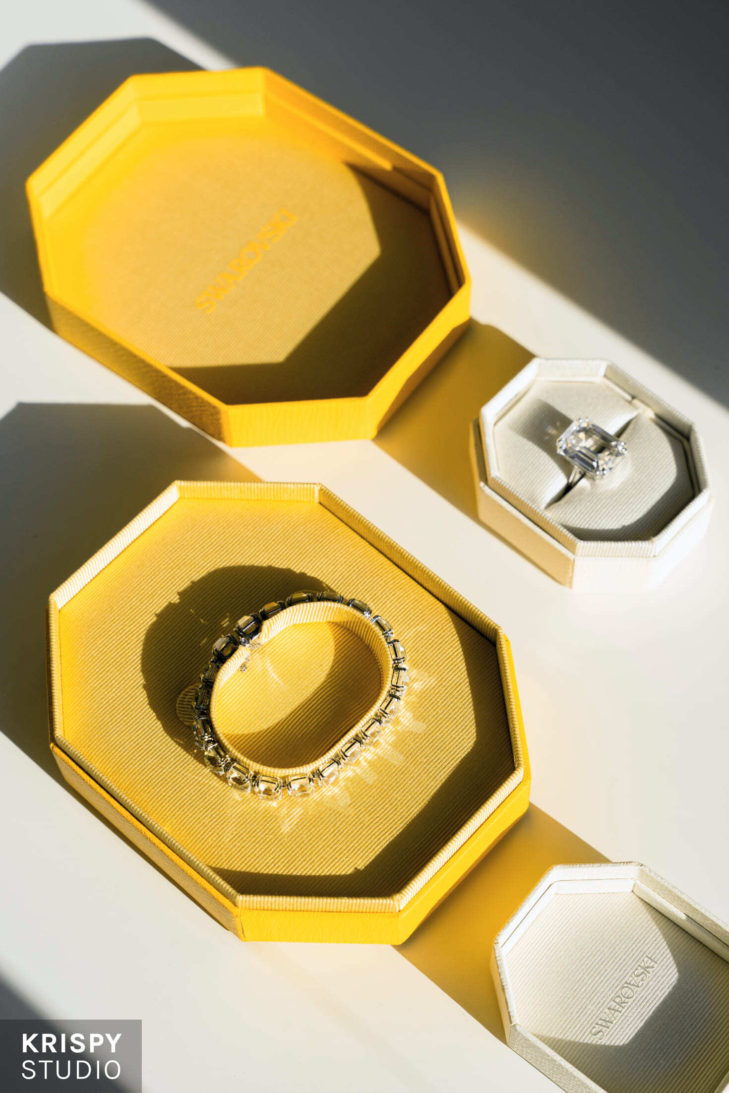 Кольцо и браслет Swarovski на белом фоне с фирменной желтой упаковкой, подчеркивающей элегантный стиль бренда.