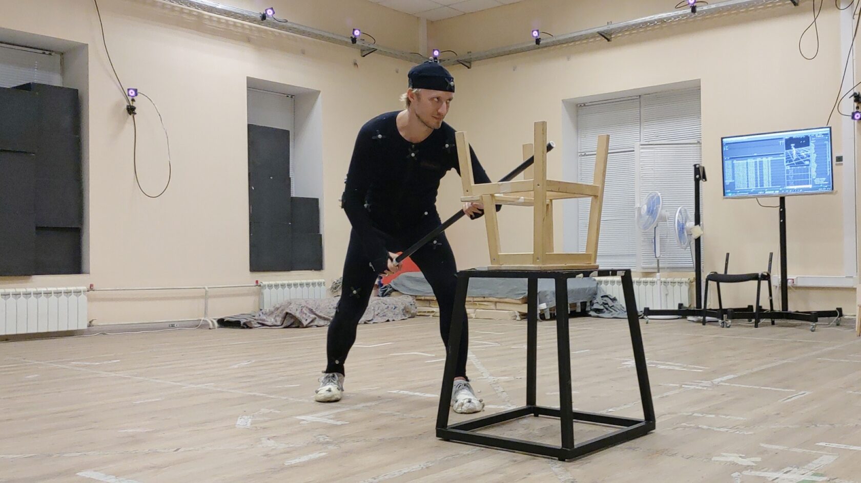 Фотография человека в мокап-костюме, который с помощью табуретки и палки изображает процесс заряда пушки