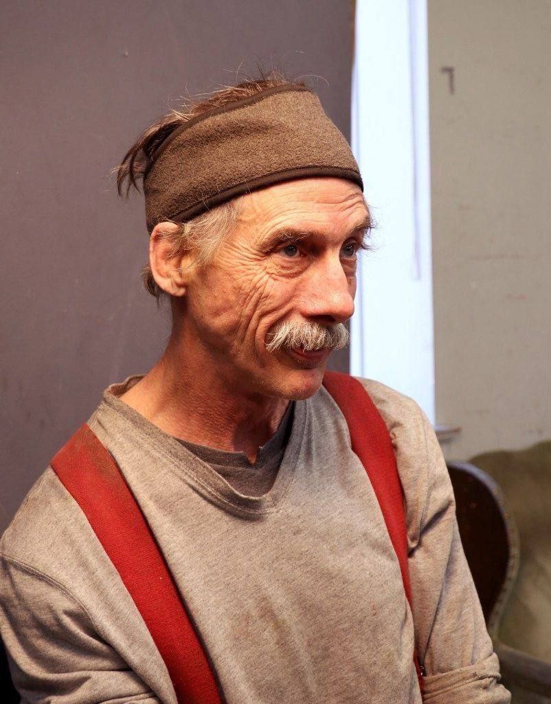 Старик с усами в серой рубашке с подтяжками
