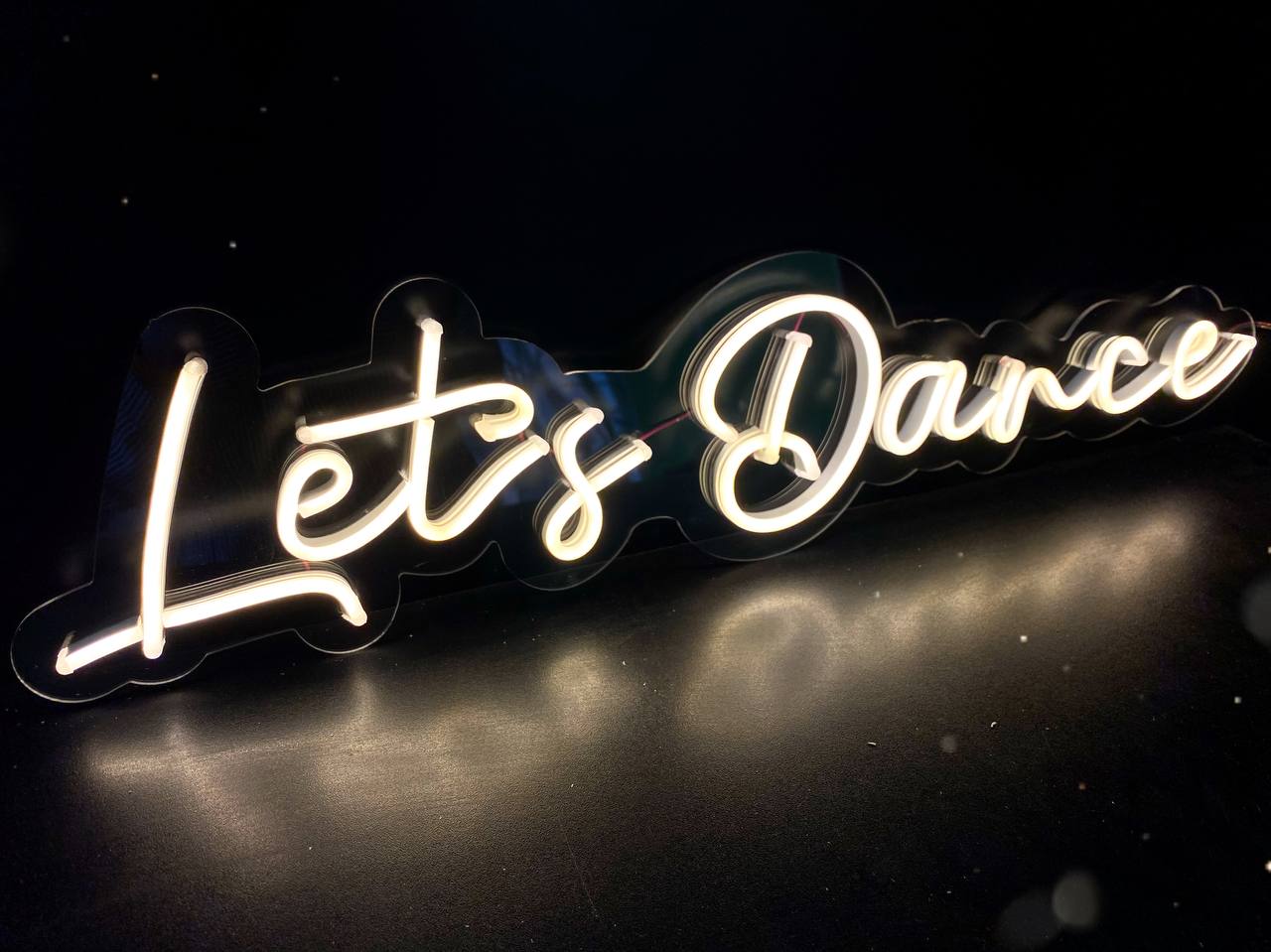 Неоновая вывеска Let’s Dance тёплого белого цвета на прозрачной подложке по контуру надписи