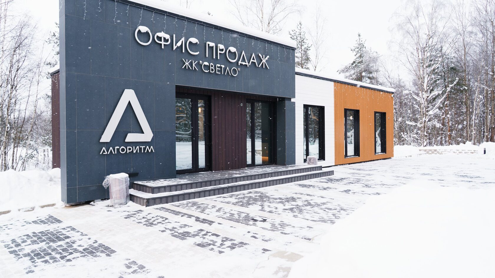 Офис продаж жилого комплекса «Светло» из пяти модулей зимой — тёмная входная группа, белый и рыжий фасады