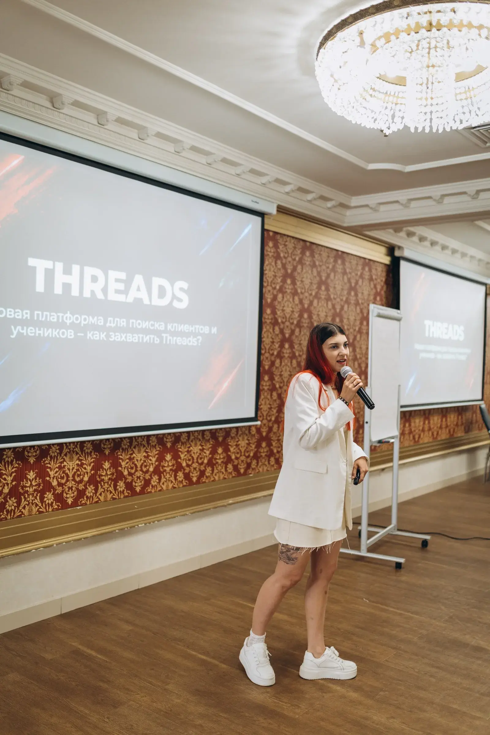 Спикер Beauty Novator 2026 выступает с микрофоном перед экраном презентации