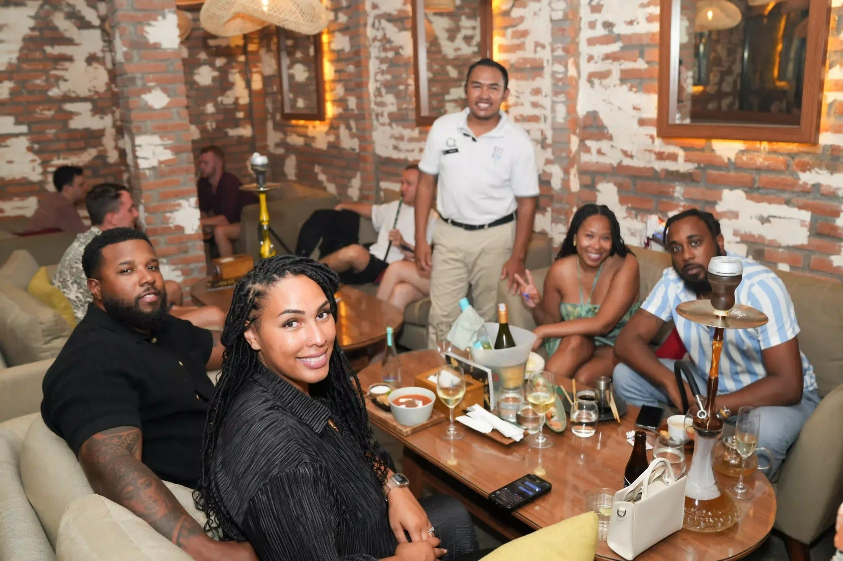 A happy group of friends toasting with wine glasses and shisha, enjoying late-night dining together as a core experience of your Bali Nightlife Guide.