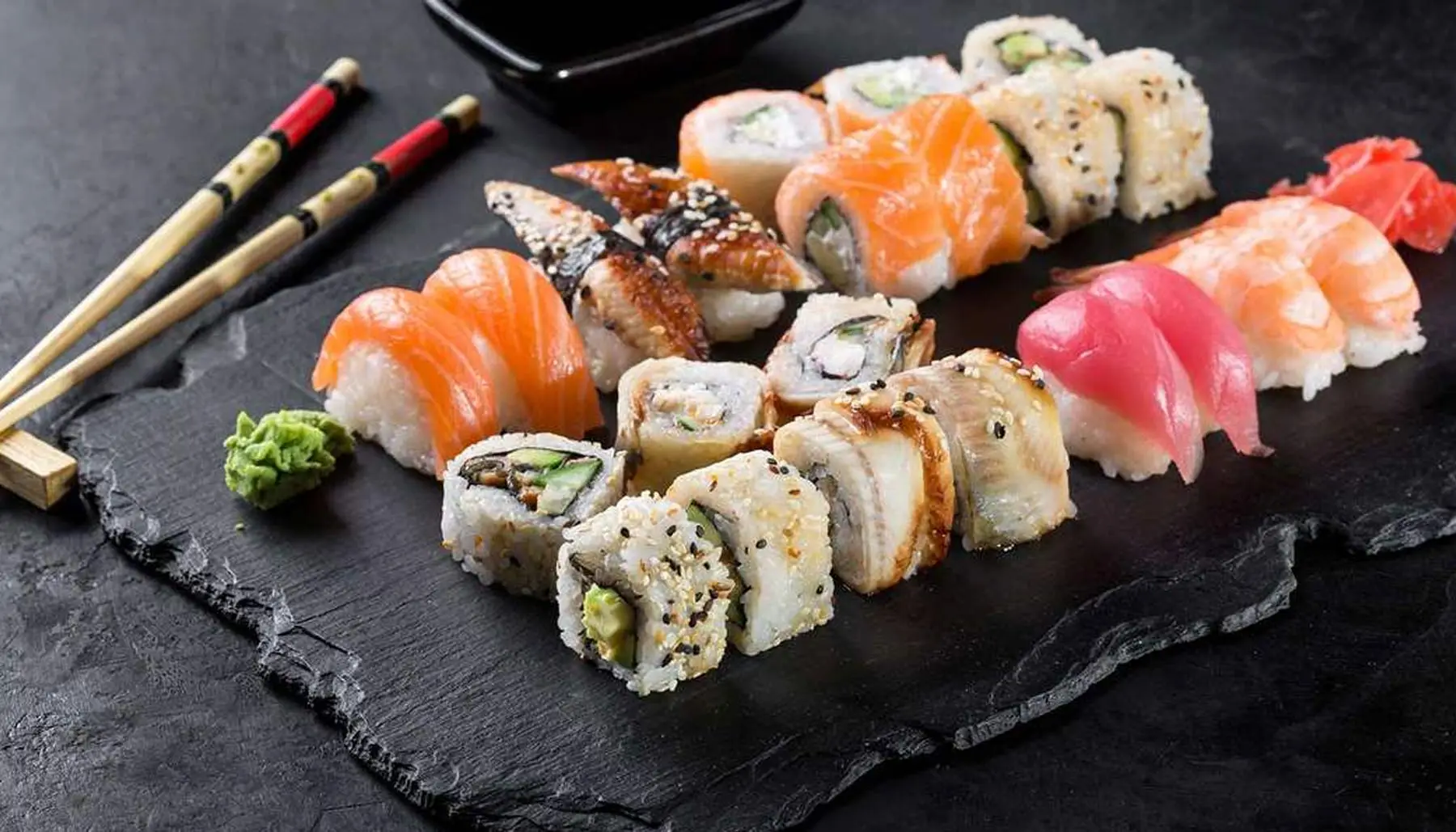A beautiful spread of fresh sushi rolls and nigiri on a black stone plate ready to be enjoyed with chopsticks. This showcases why its considered some of the best sushi in Seminyak.