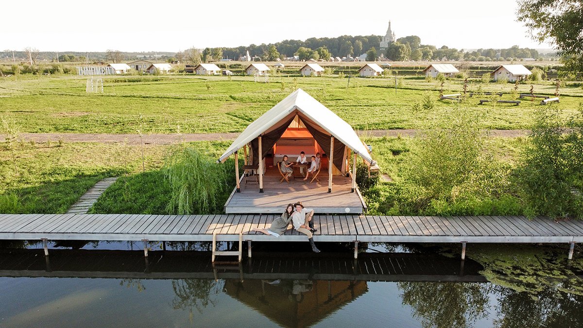 Guests at a table by a safari tent on the deck over the water at Ostrov Glamping