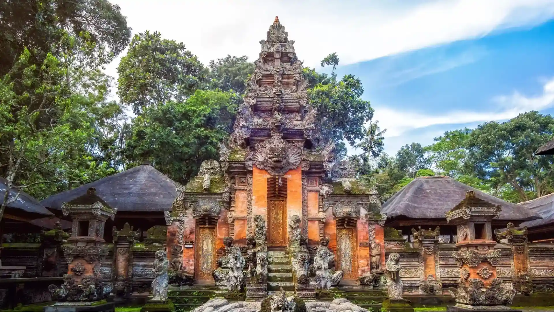 The majestic and highly detailed red brick gates of the Prajapati Temple, surrounded by lush tropical greenery inside the sanctuary of Monkey Forest Ubud.