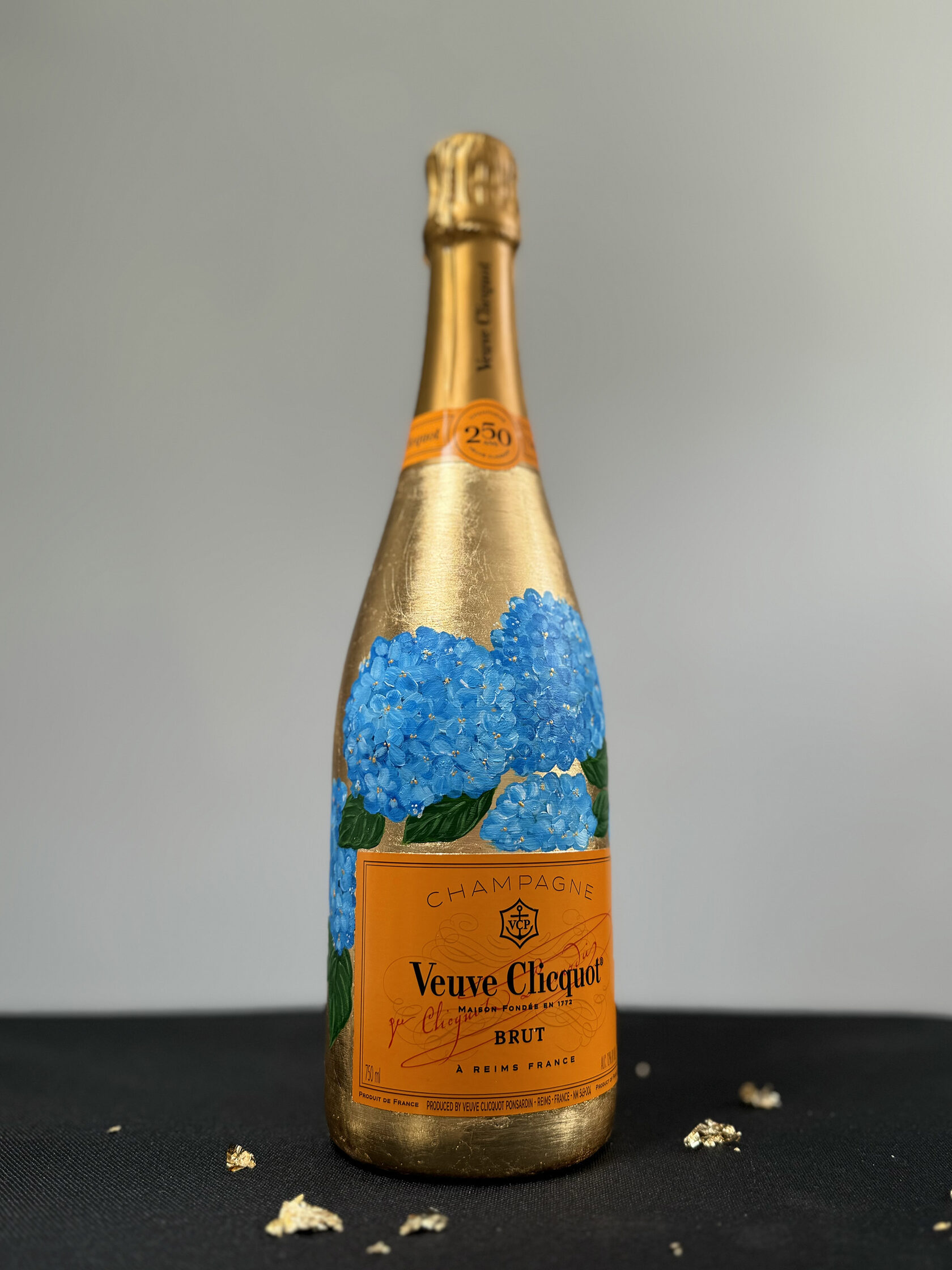 Custom hand-painted gold Veuve Clicquot champagne bottle featuring vibrant blue hydrangea artwork by Julia Razz.