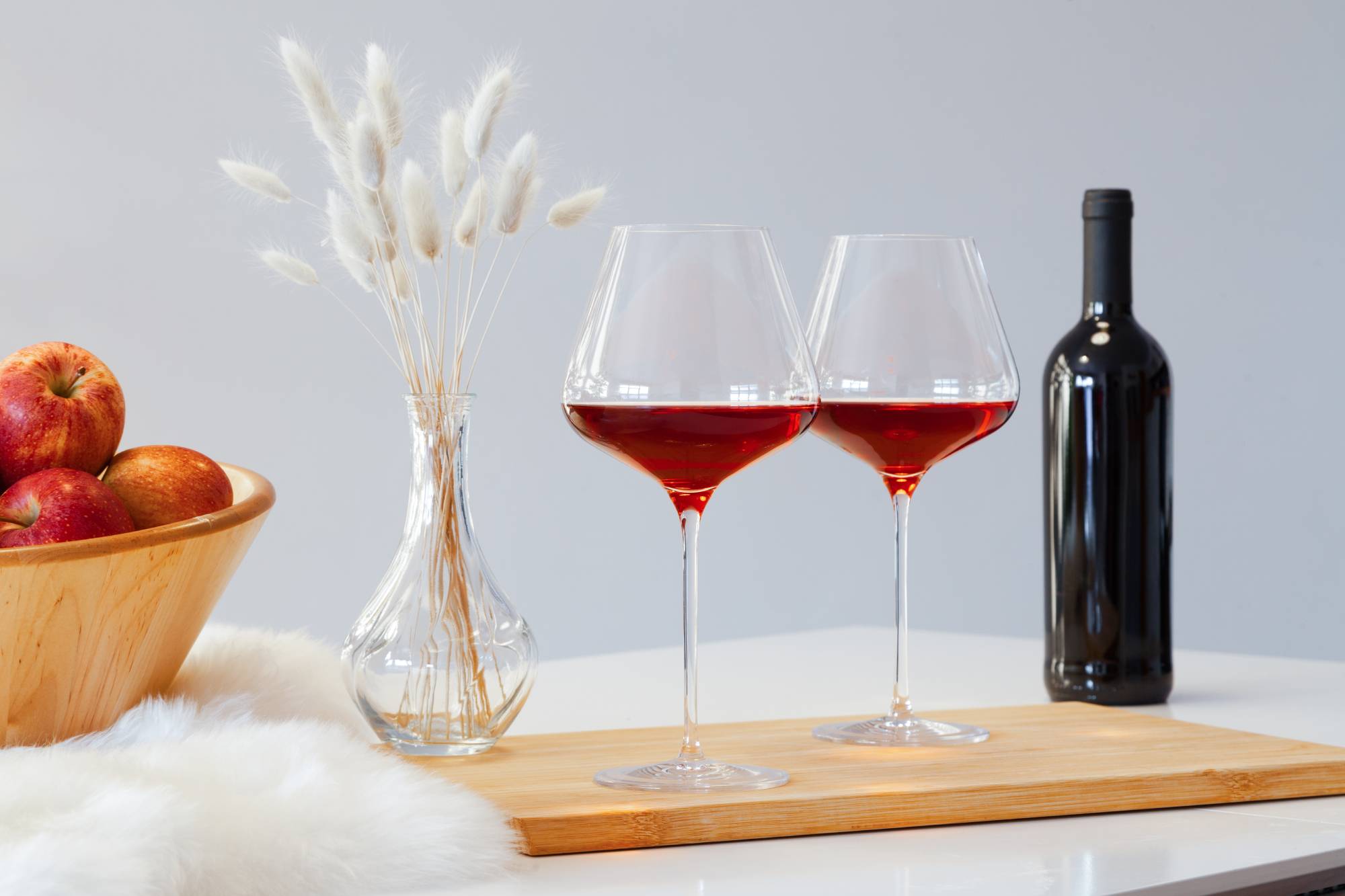 Bottle on the table. Овальный столик в интерьере комнаты с бокалами красного вина. Деревянные кубки вино. Всему виной вино. Вино красное на столе с белой скатертью.