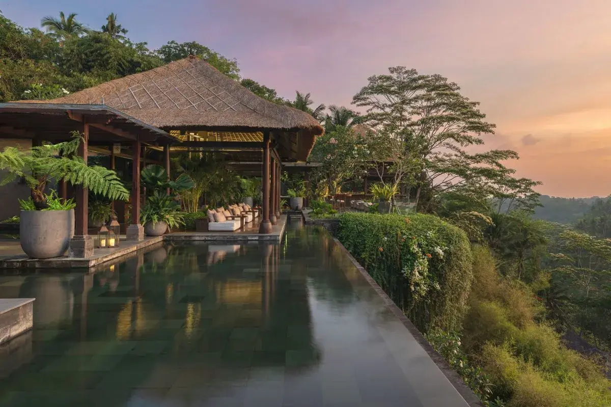 Luxurious infinity pool reflecting a traditional thatched-roof pavilion at Mandapa, a Ritz-Carlton Reserve, offering stunning sunset views over the Ubud jungle.