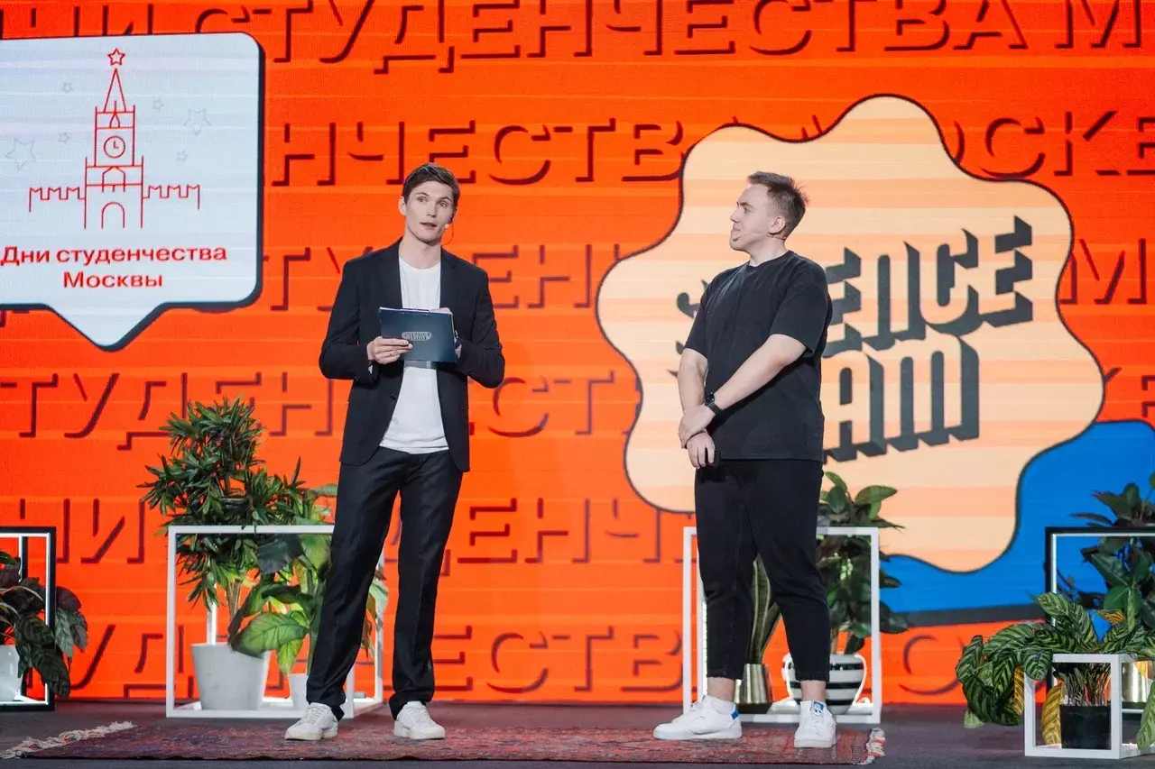 Ведущий с папкой и участник на сцене Science Slam; на фоне надпись «Дни студенчества Москвы»
