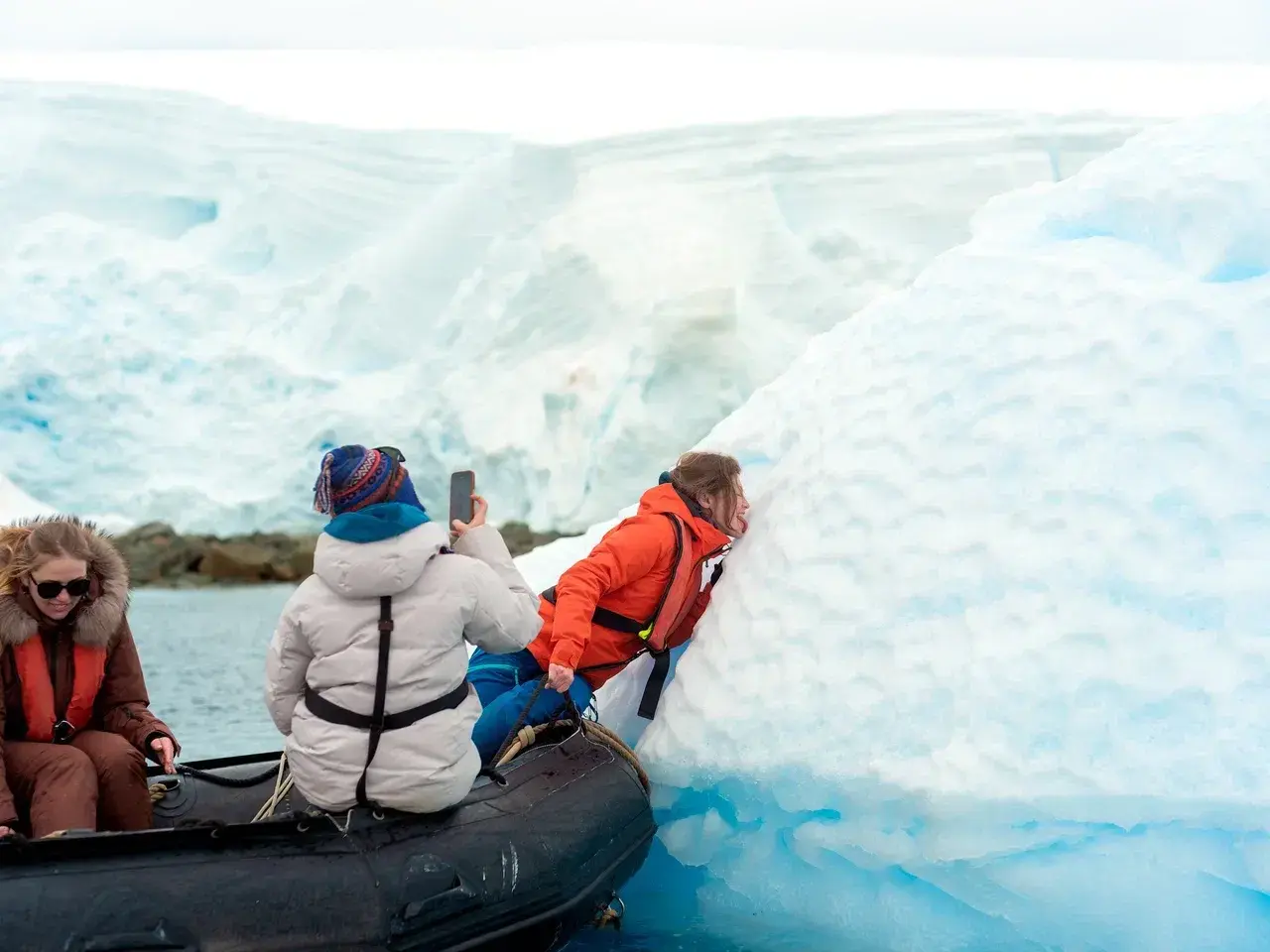 Antarctica expedition participants exploring a massive blue iceberg by Zodiac boat during a small-group polar adventure.