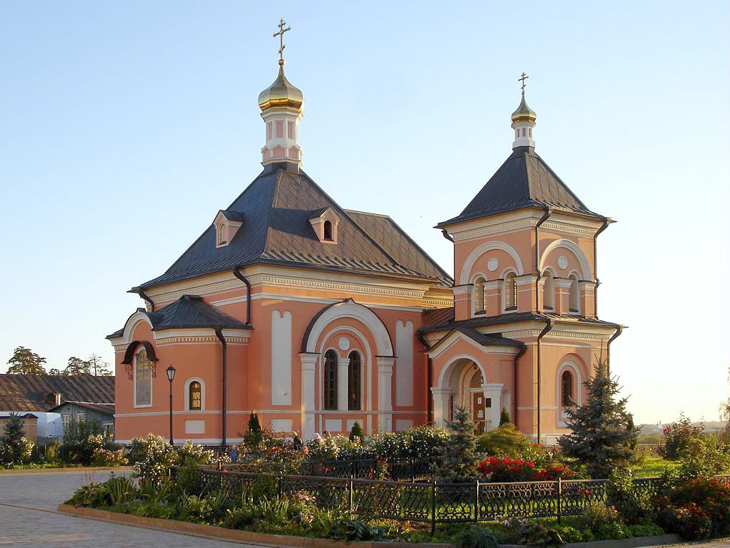 Кирпично-розовый храм с золотыми главками и клумбами перед ним, Оптина Пустынь