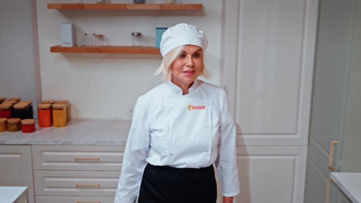Женщина в белом поварском кителе и колпаке на светлой кухне, на полке банки — кадр из ролика «Одоевских консервов»
