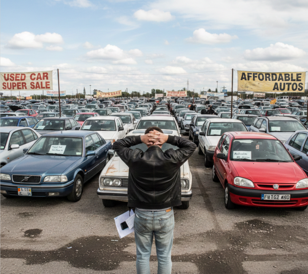 Человек стоит спиной, выбирает поддержаный автомобиль из большого ассортимента