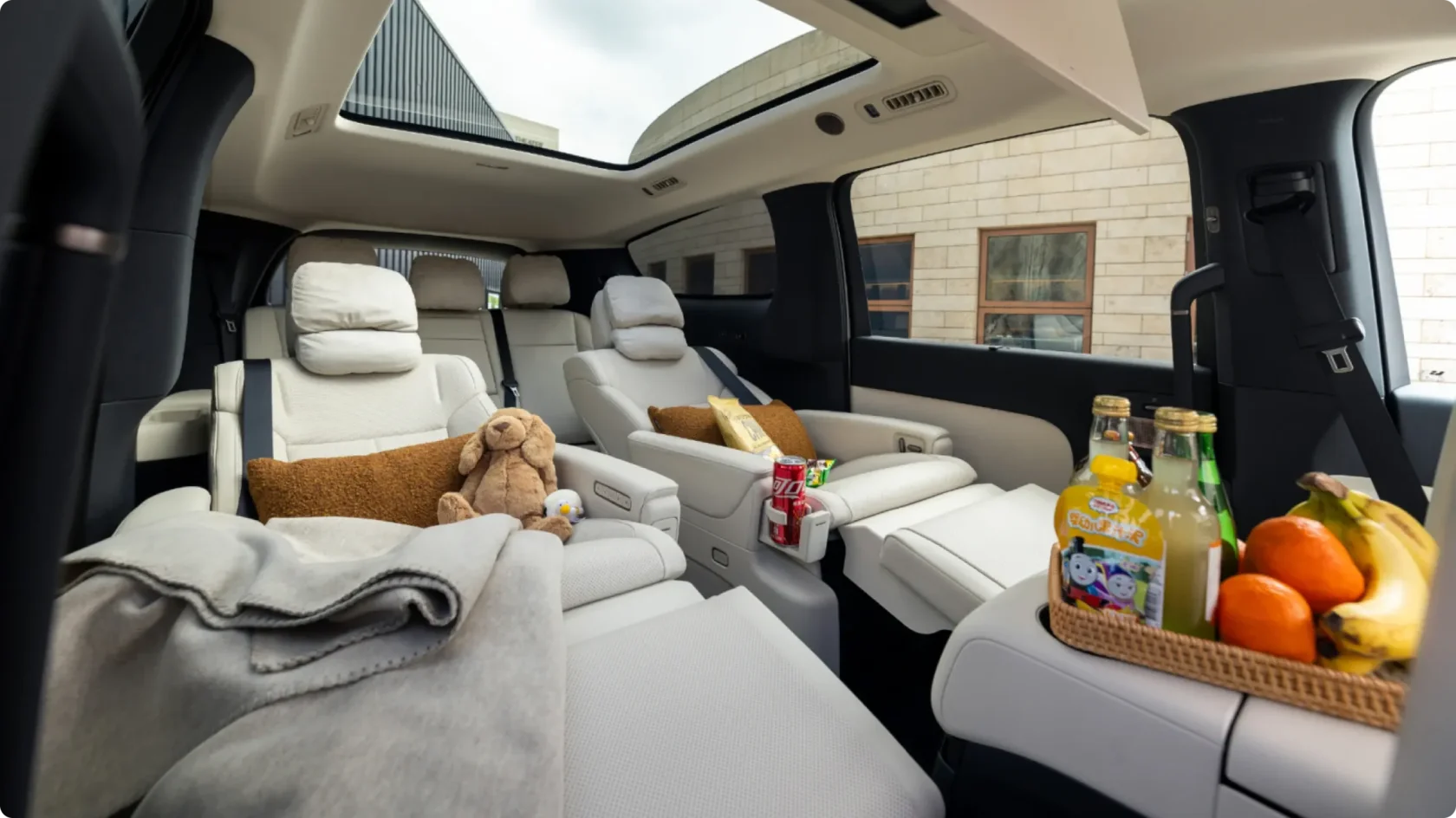 Премиальный салон Li Auto Mega Home: разложенные кресла второго ряда с мягкими подушками и пледами, панорамная крыша, корзина со свежими фруктами и напитками в просторном интерьере минивэна.