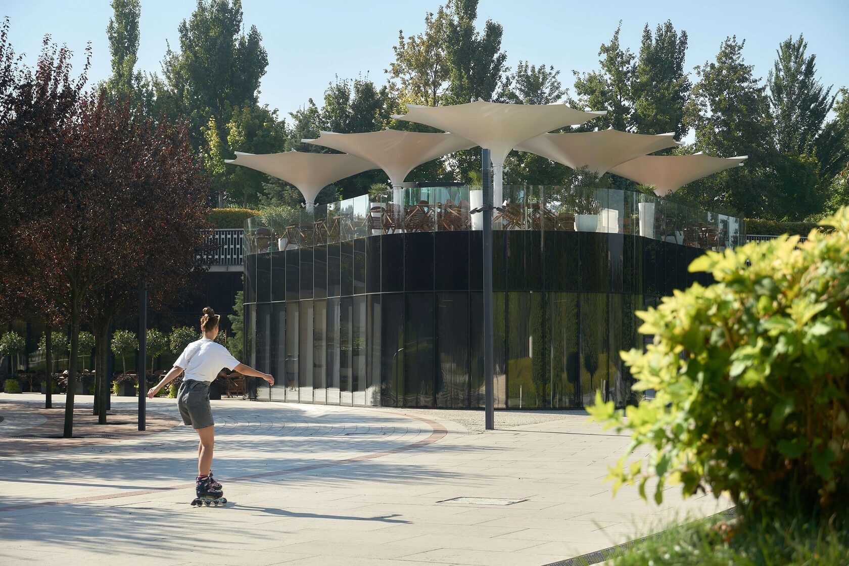 Парк Краснодар: девушка на роликах рядом с современным павильоном и зелёными насаждениями.