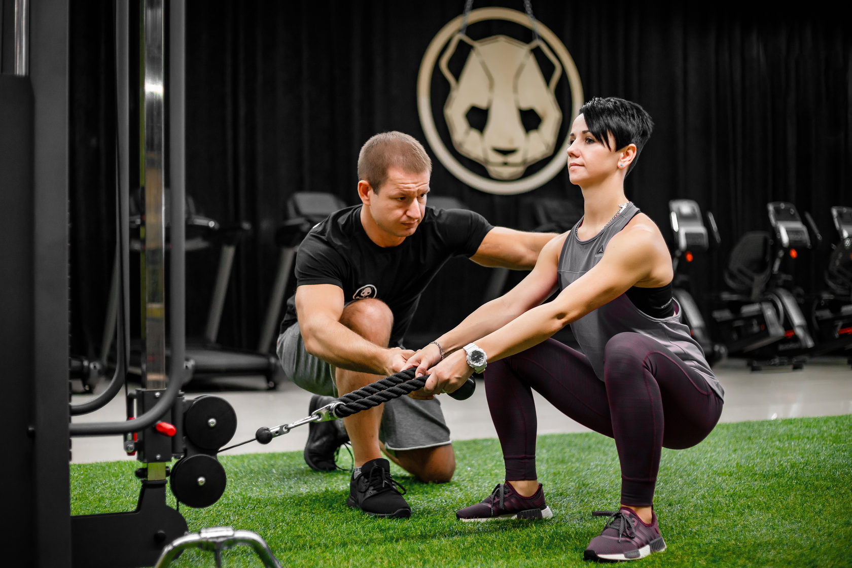 Тренер помогает освоить упражнение в тренажёрном зале Panda Sport